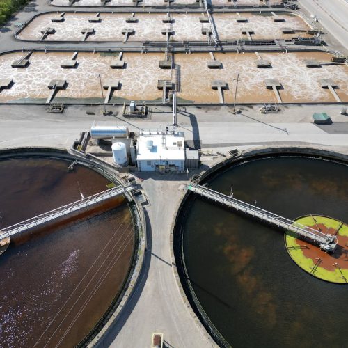 Aerial shot of an industrial water treatment plant with large circular tanks.